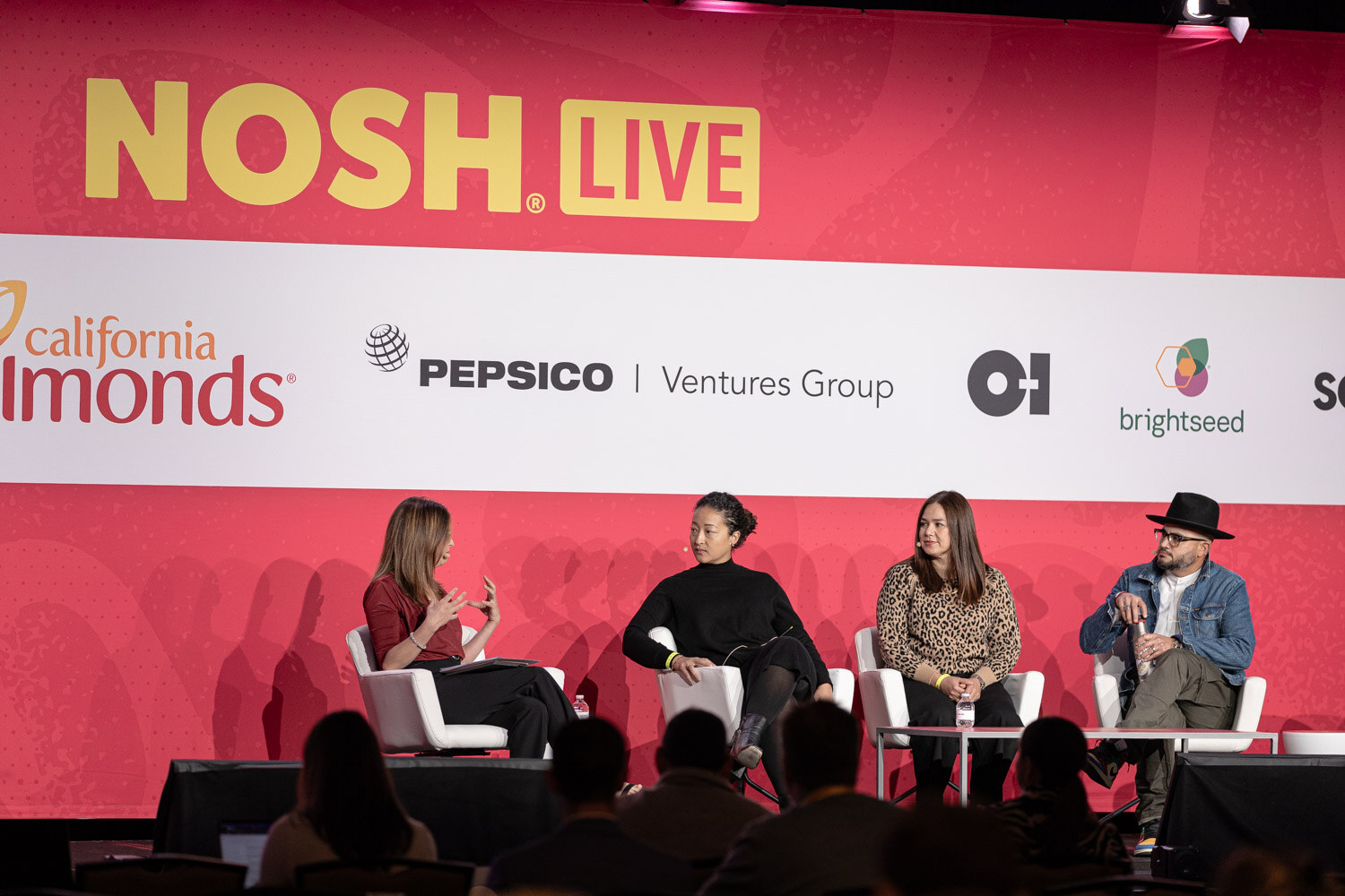 Four people in white chairs on stage in front of California Almonds and Pepsico Ventures Group signs.