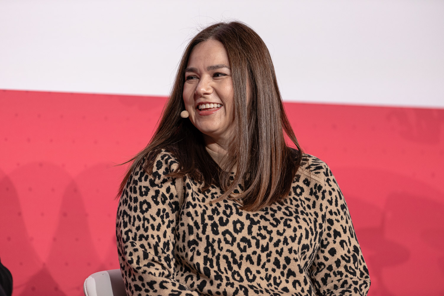 A woman with long hair in a leopard-print sweater laughing on stage.