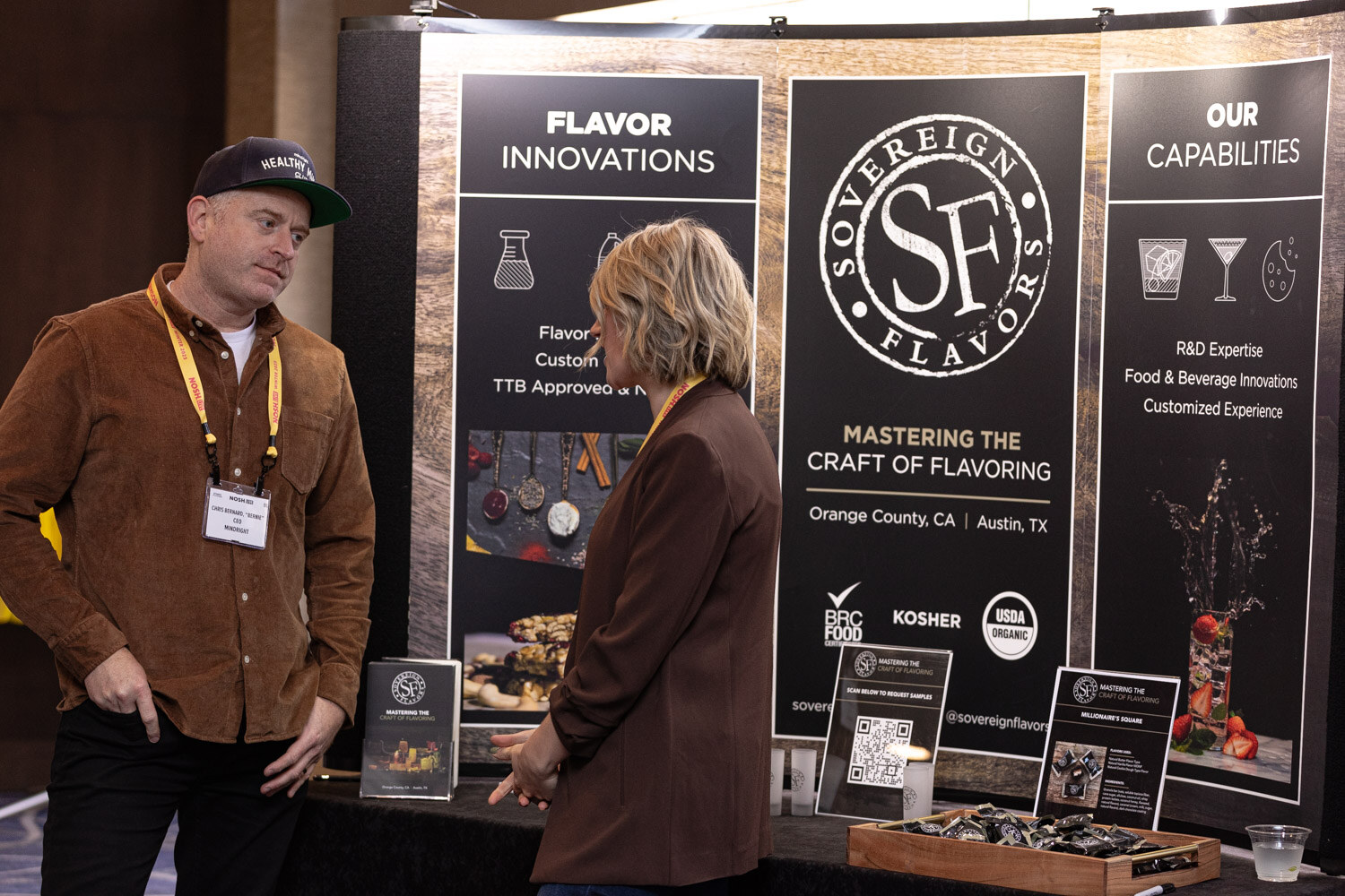 Two people in conversation in front of a black Sovereign Flavors display board.
