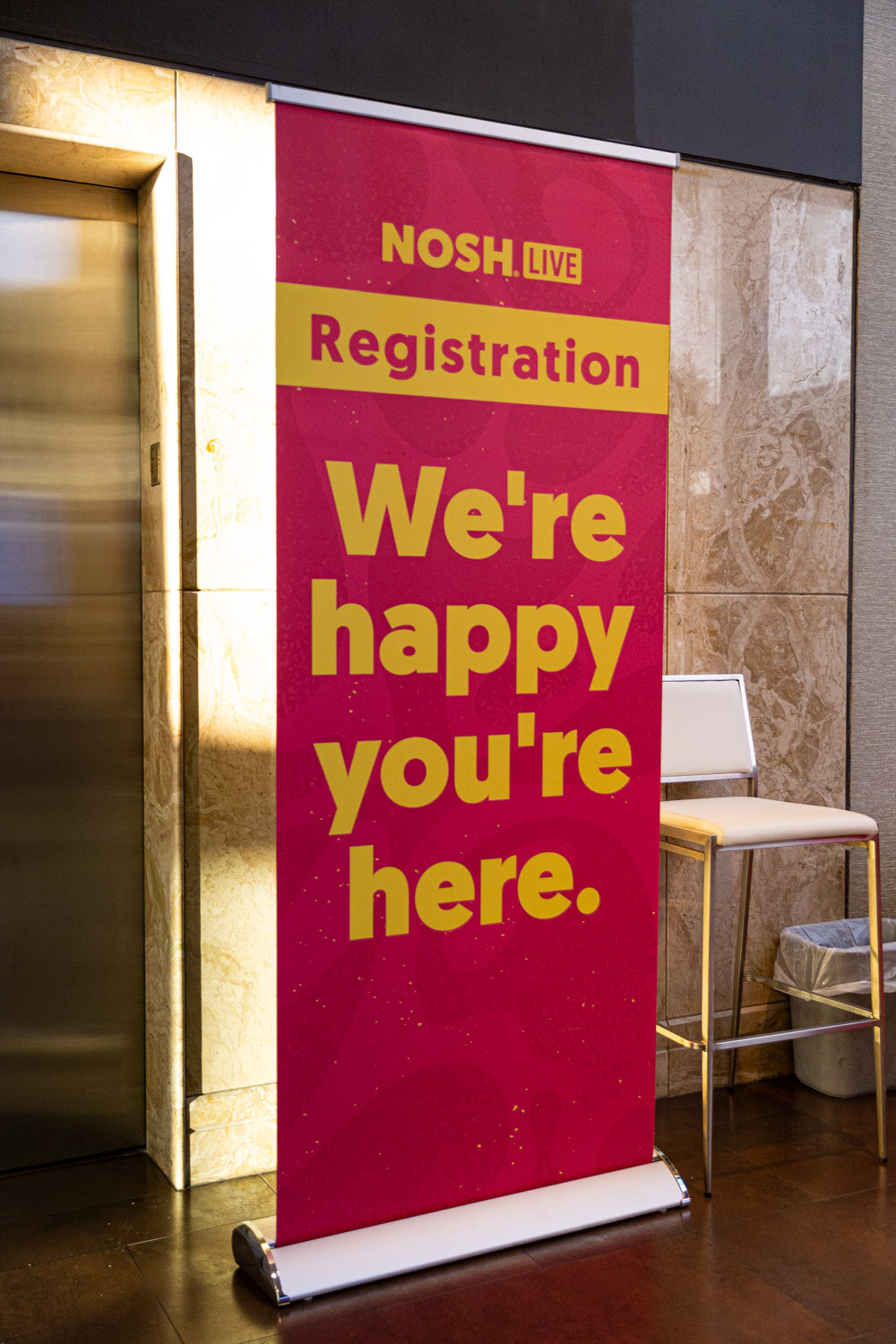 A pink and yellow standing banner reading Registration, We are happy you are here, next to an elevator.