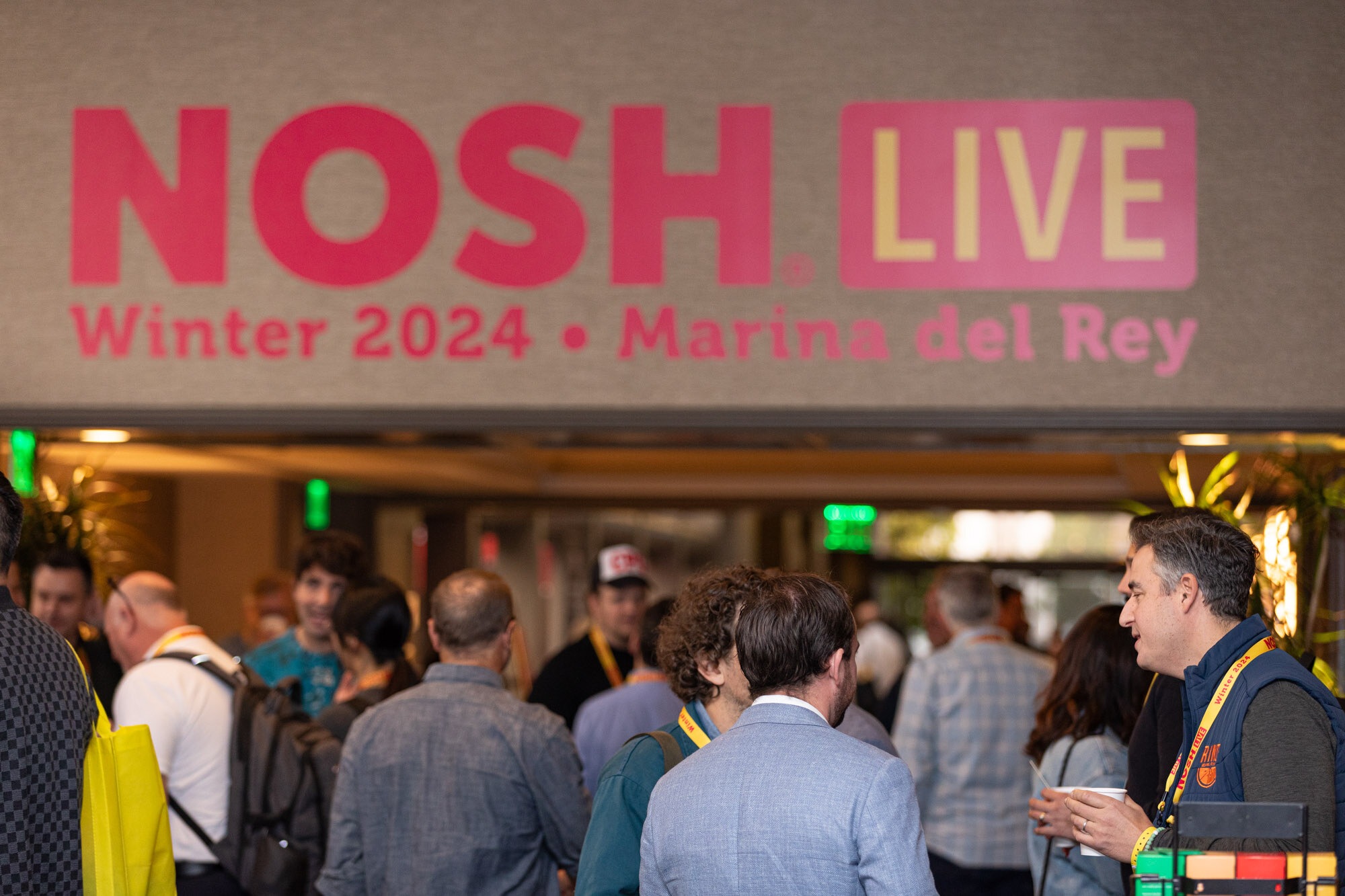 A crowd of lanyard-wearing attendees beneath a lit sign reading Nosh Live Winter 2024 Marina del Rey.