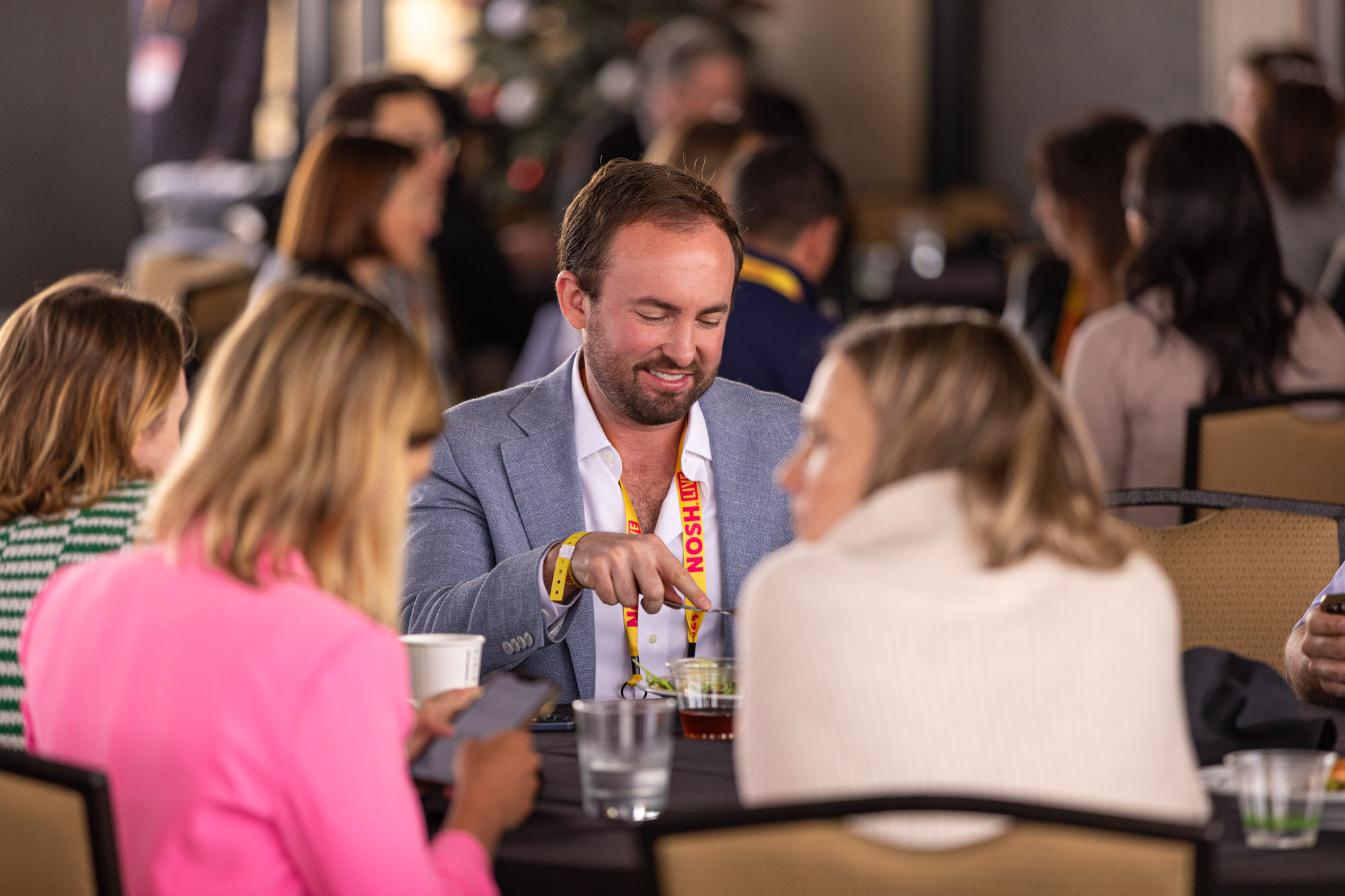 A man in a light blazer smiling at a table with several people eating lunch.