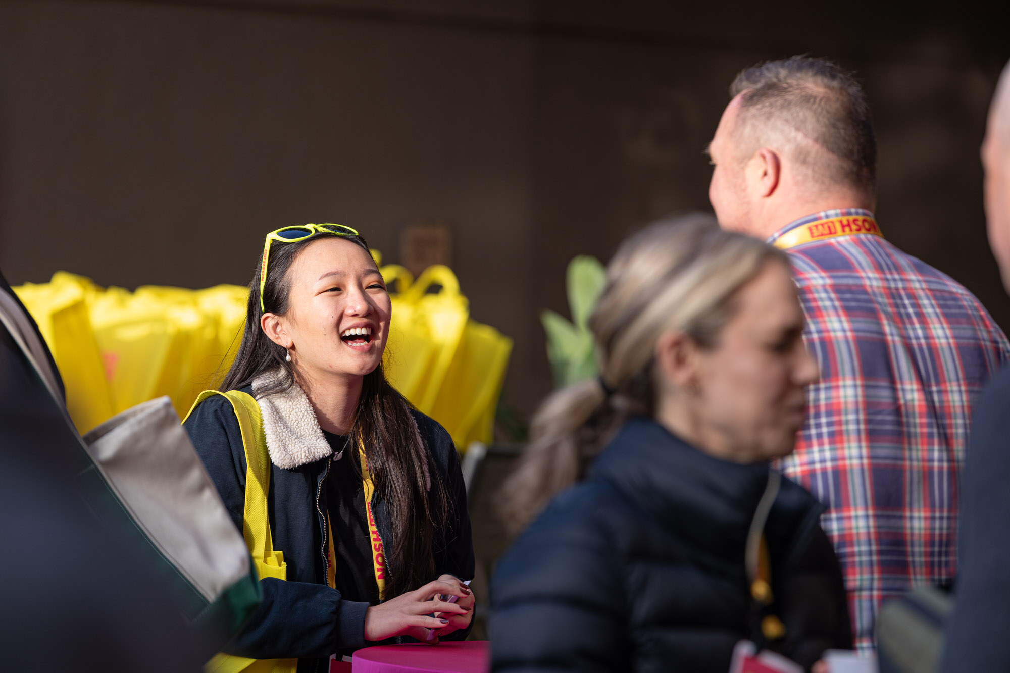 A woman laughing with yellow sunglasses on her head and a lanyard around her neck.