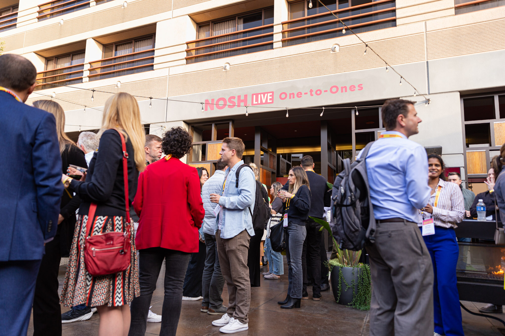 Attendees standing outdoors in front of a red Nosh Live sign, some with drinks.