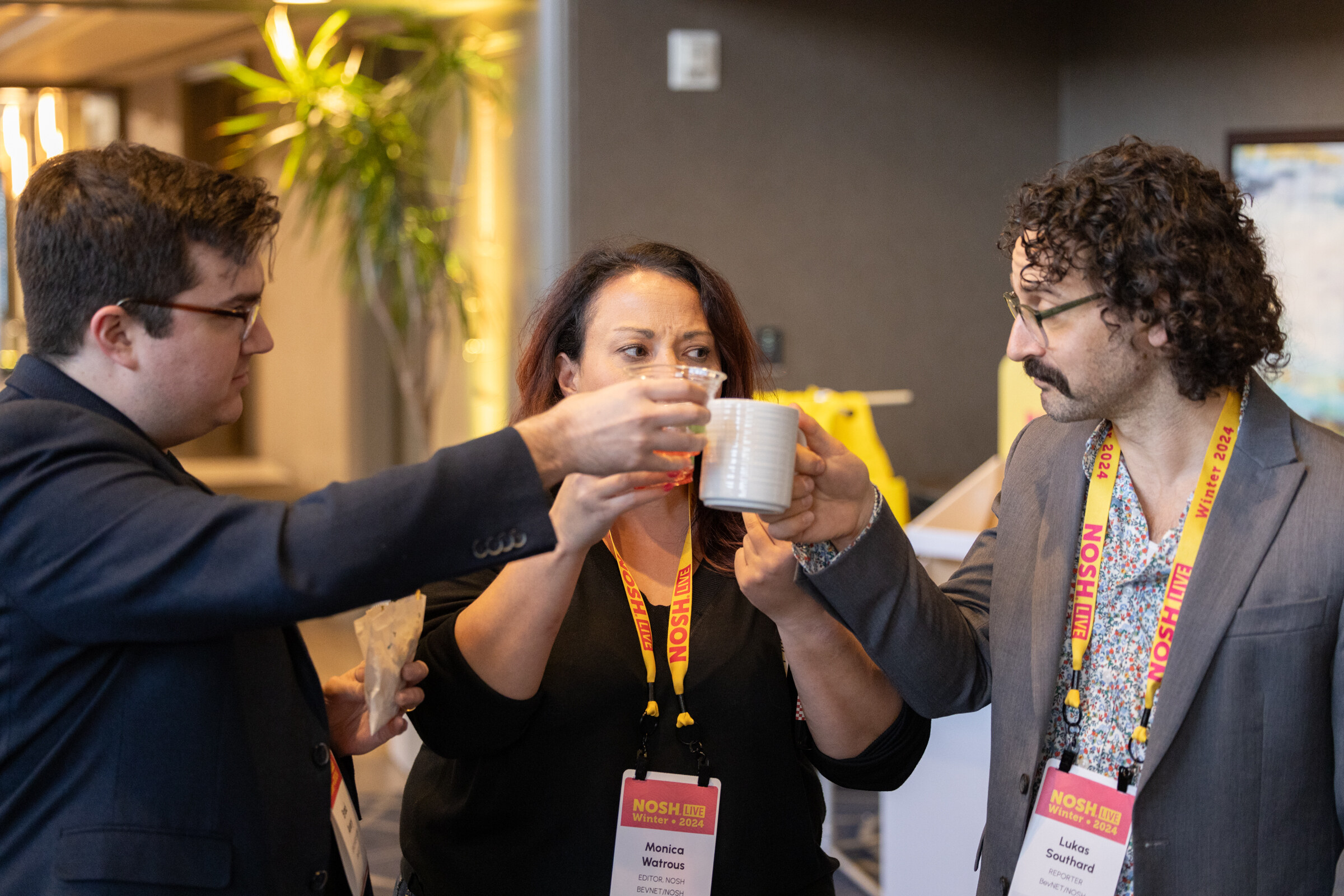 Three people with badges clinking cups in a hallway.