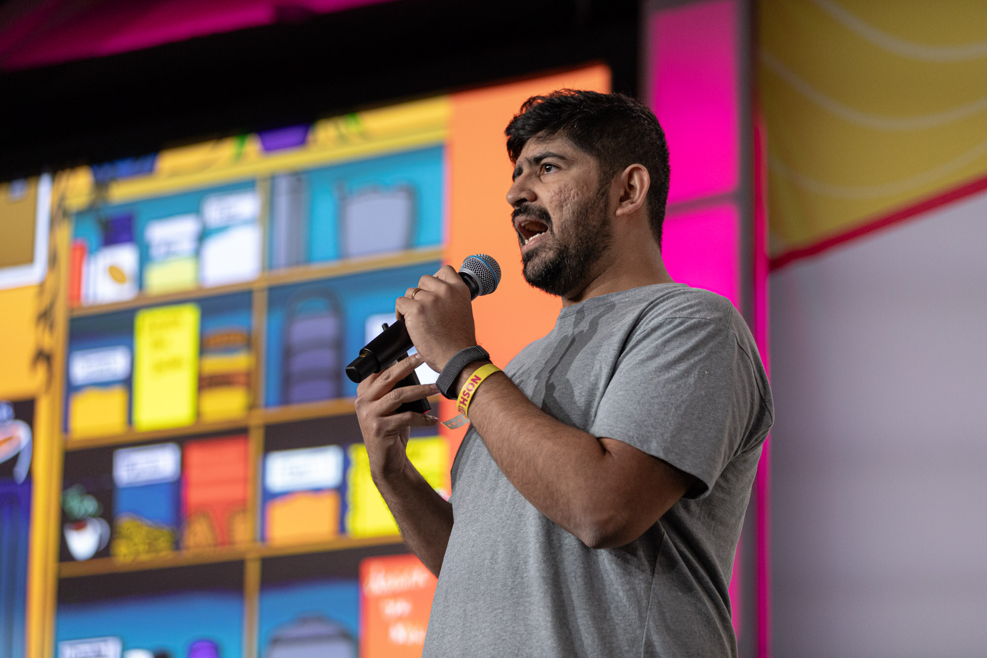 A man in a gray t-shirt gesturing toward a slide of colorful pantry items on a stage with a Bay State Milling sign behind him.