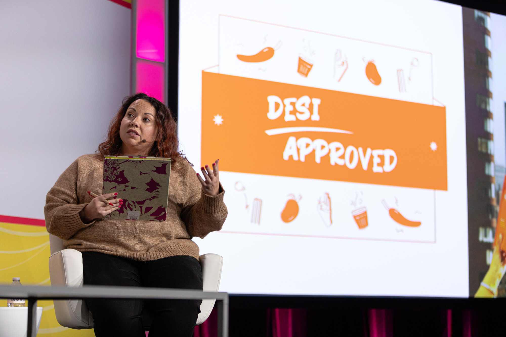 Wide view of judges seated in white chairs with a screen showing a product slide at the left.