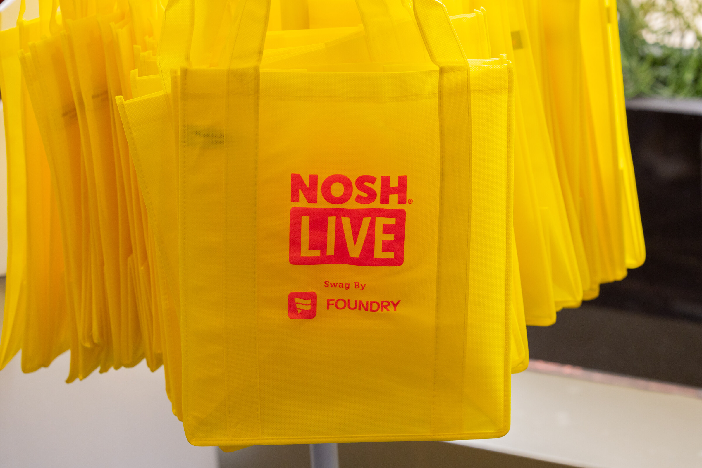 A cluster of yellow reusable bags printed with Nosh Live and Swag by Foundry.