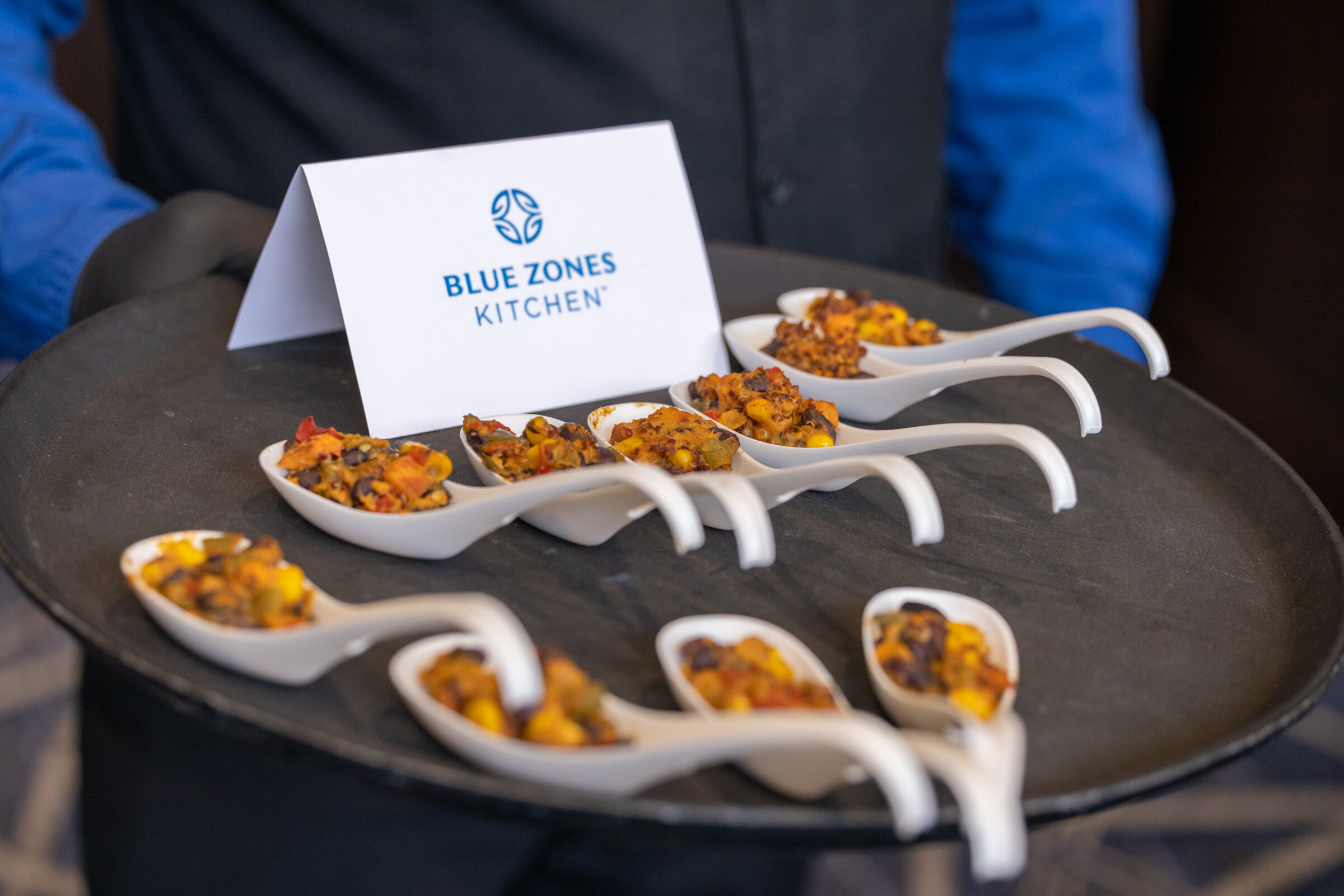A black tray with small white spoons of food and a card reading Blue Zones Kitchen.