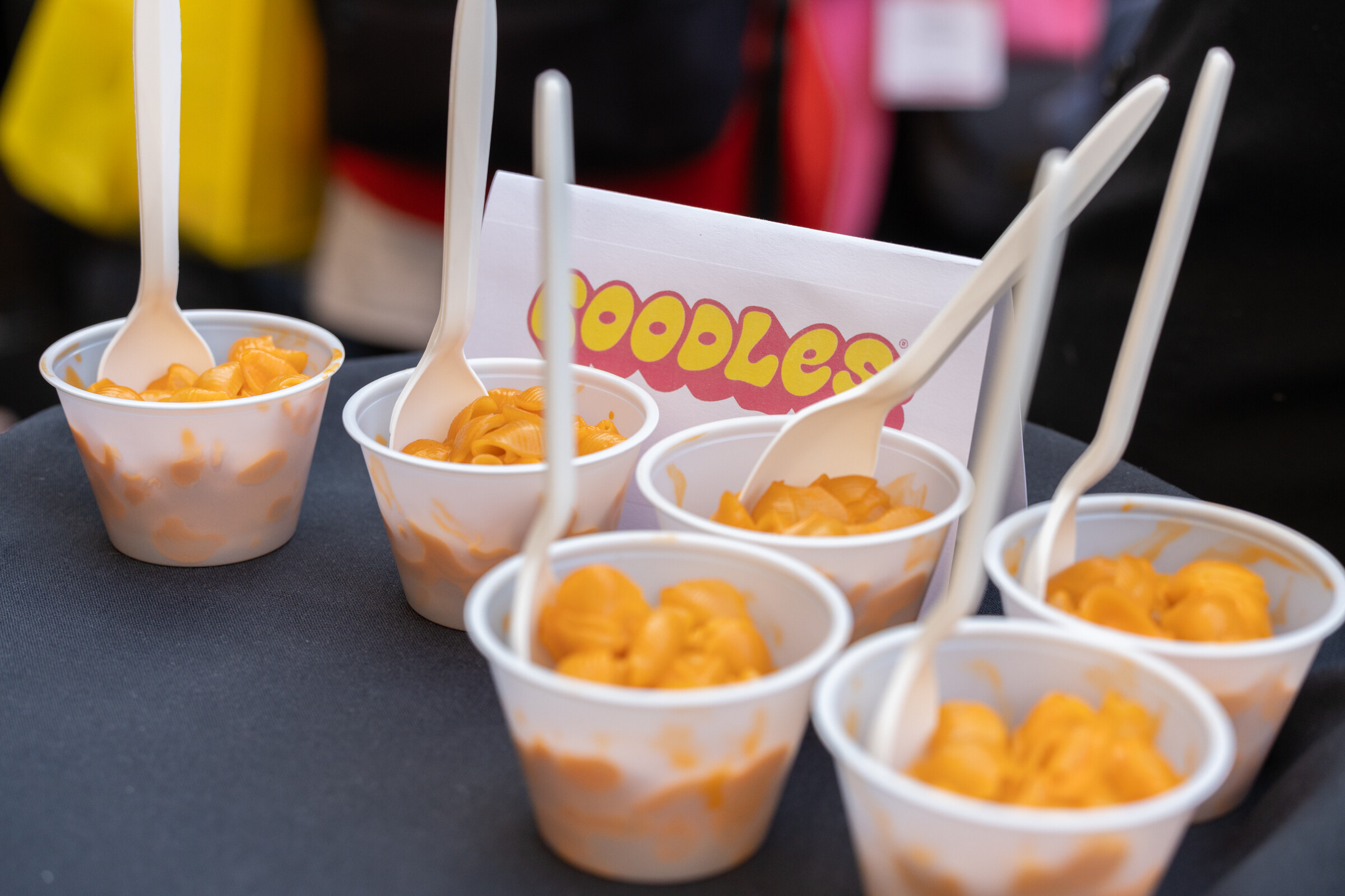 Five cups of macaroni and cheese with white forks and a Goodles sign.