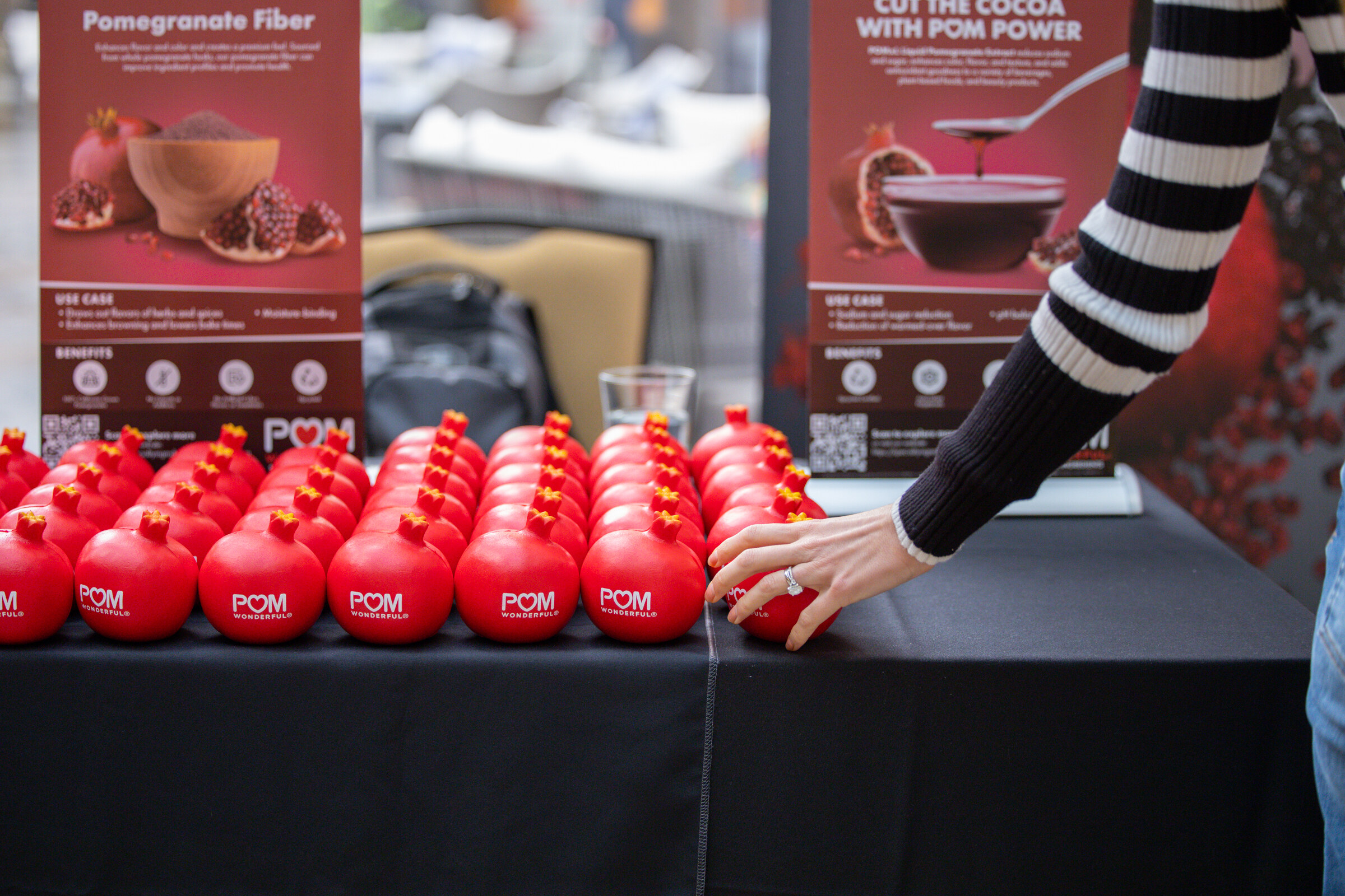 A long table of red pomegranate-shaped stress balls with POM Wonderful logos and two Pomegranate Fiber banners.
