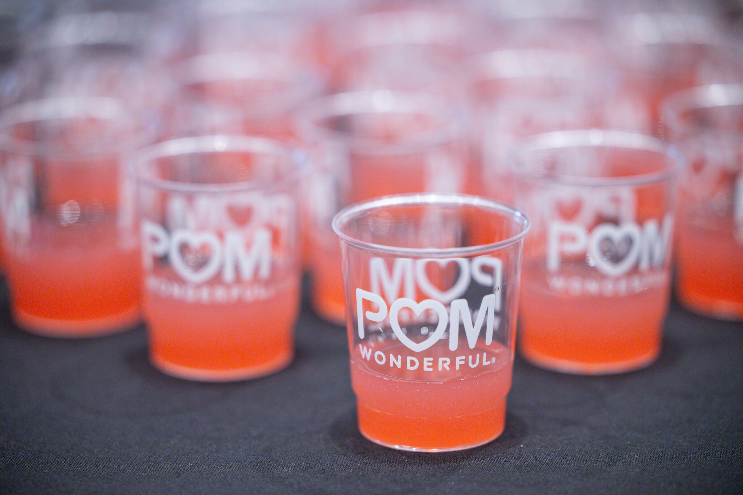 Rows of clear cups printed with POM Wonderful filled with an orange-red drink.