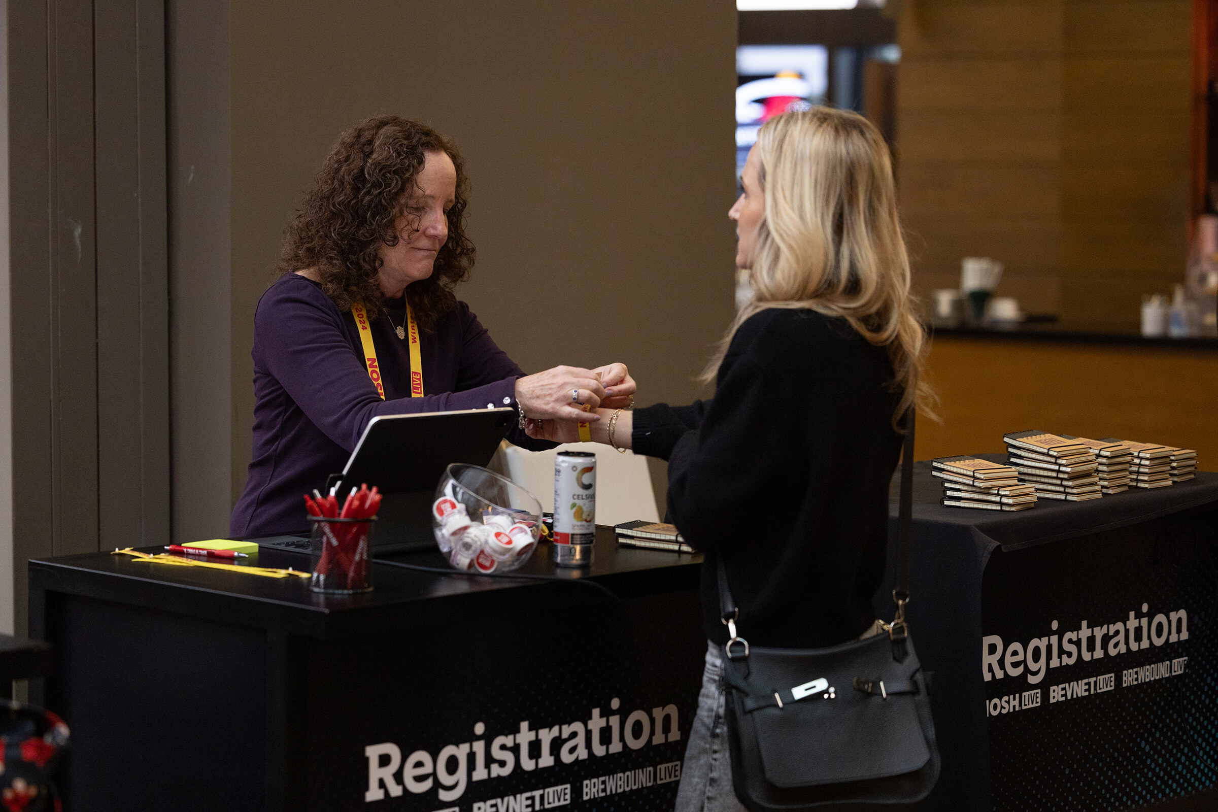 A woman at a registration table fastening a wristband on an attendee's wrist.
