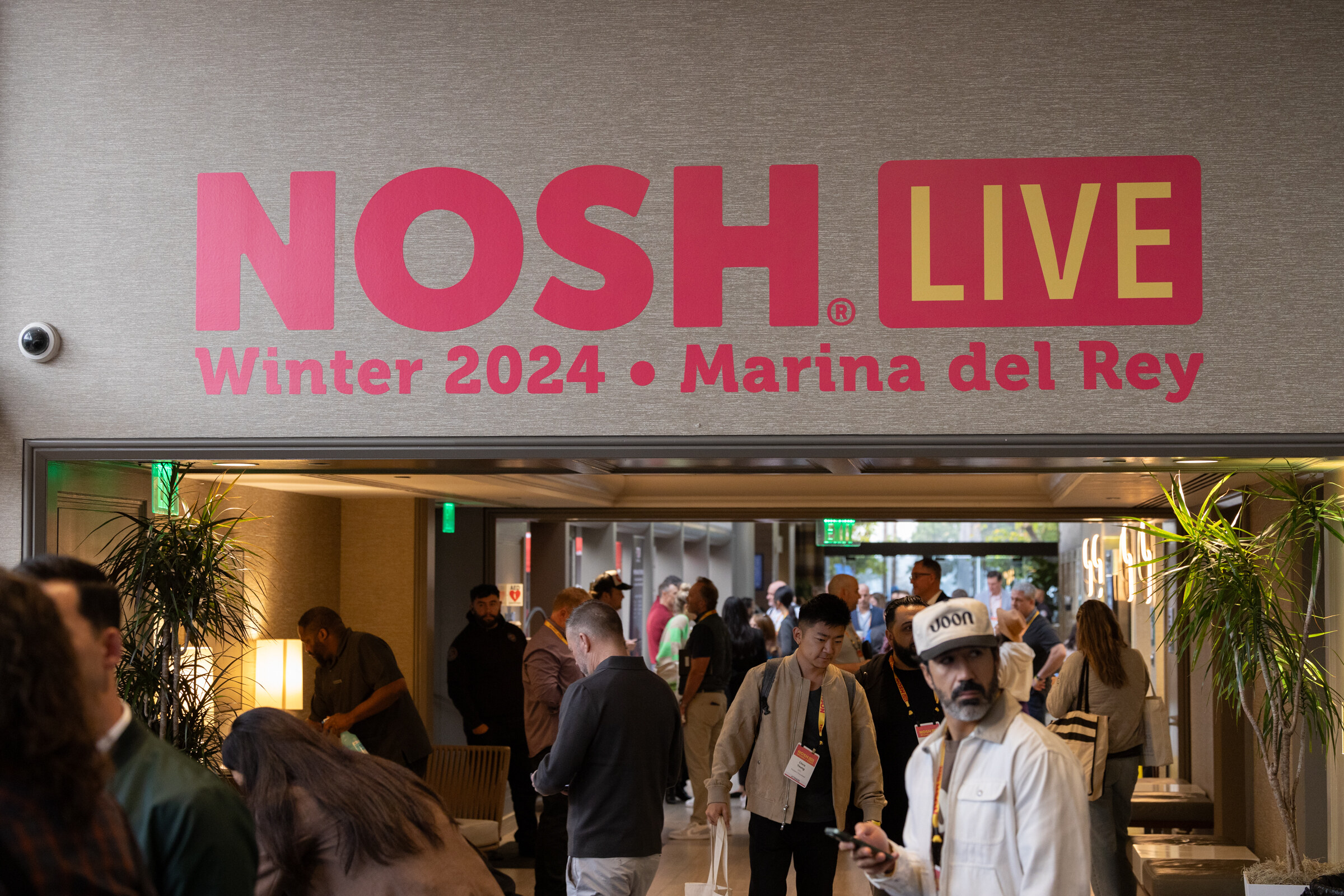 A pink Nosh Live Winter 2024 Marina del Rey sign above a corridor with attendees walking in.