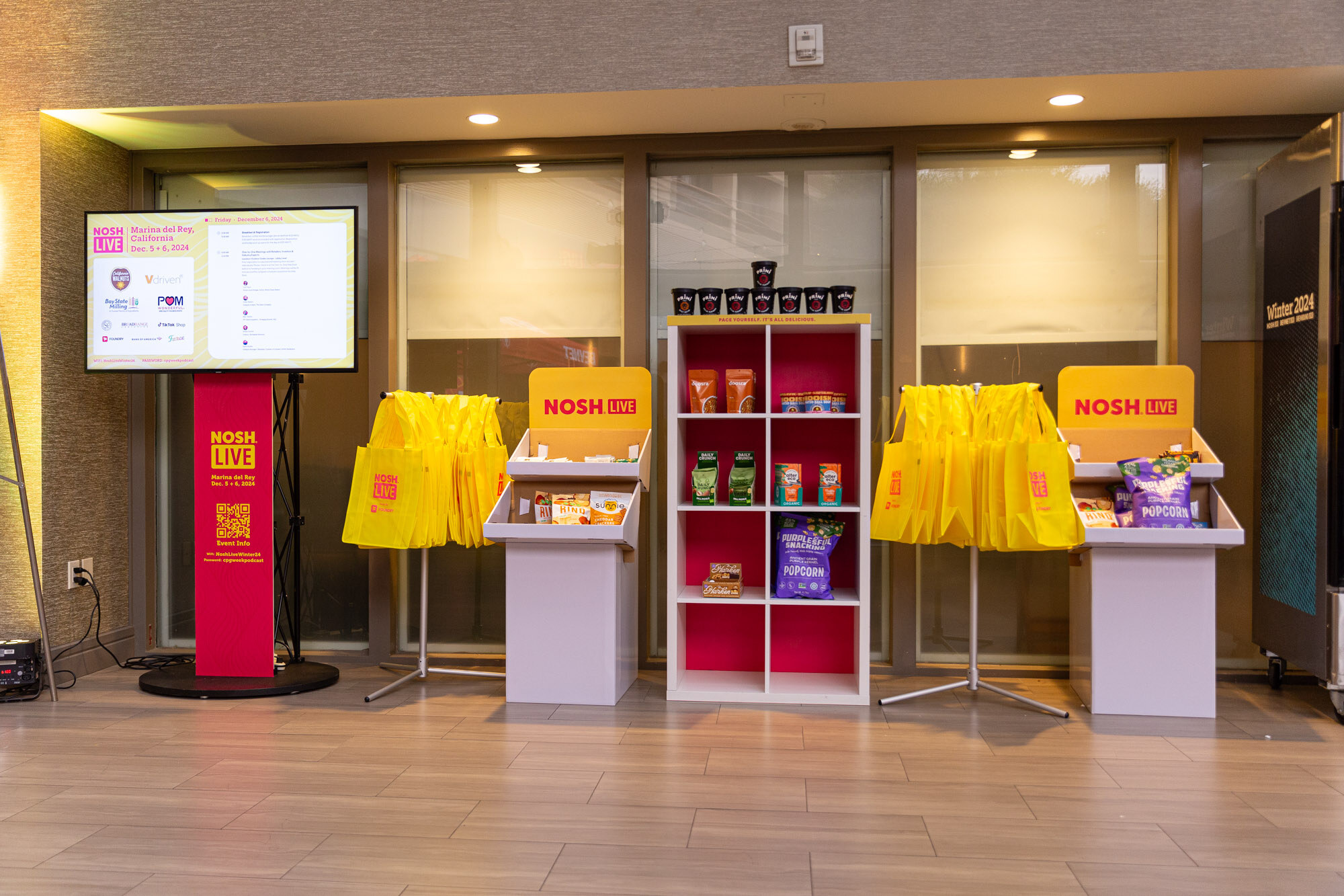 Wide view of a lobby display with yellow bags, a monitor and shelves of products.
