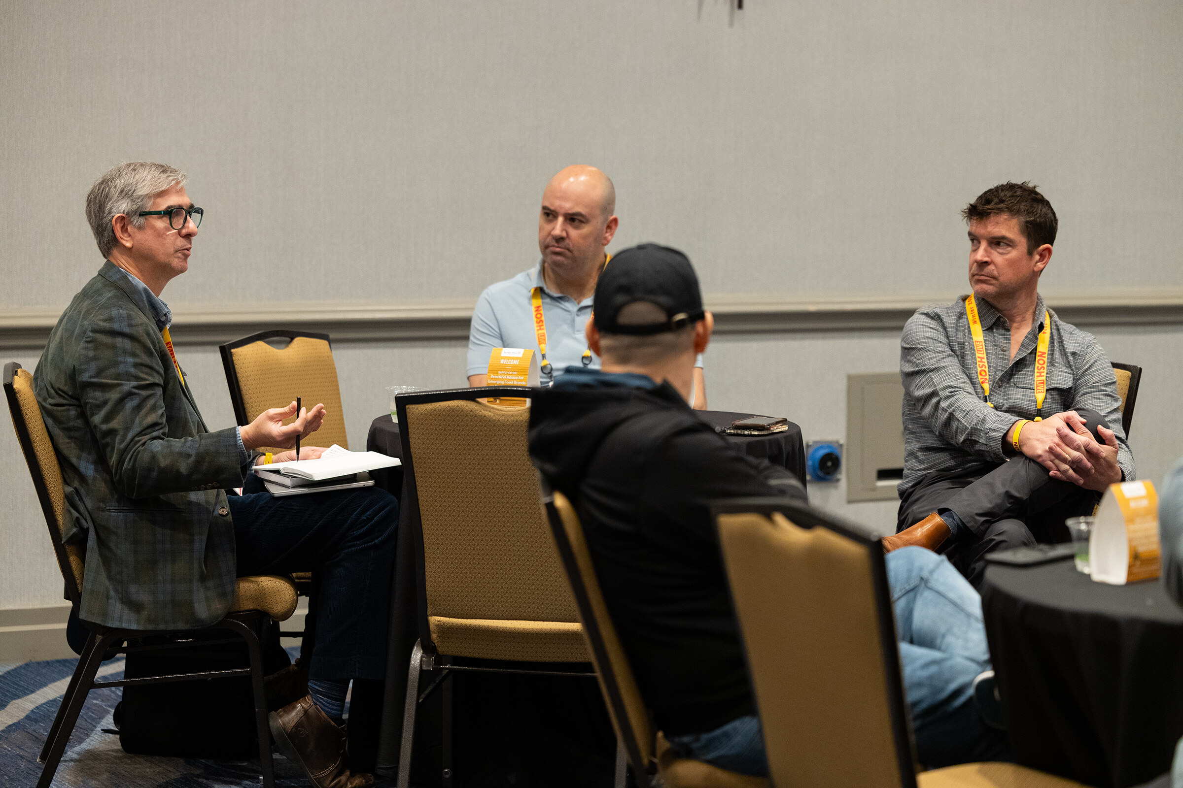Wide view of three men seated at a table in a hotel meeting room.
