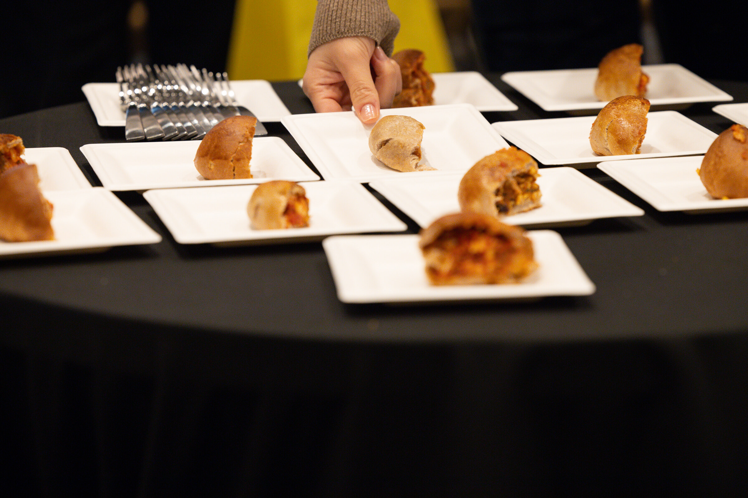 Square white plates with halved empanadas on a round table with a black cloth.