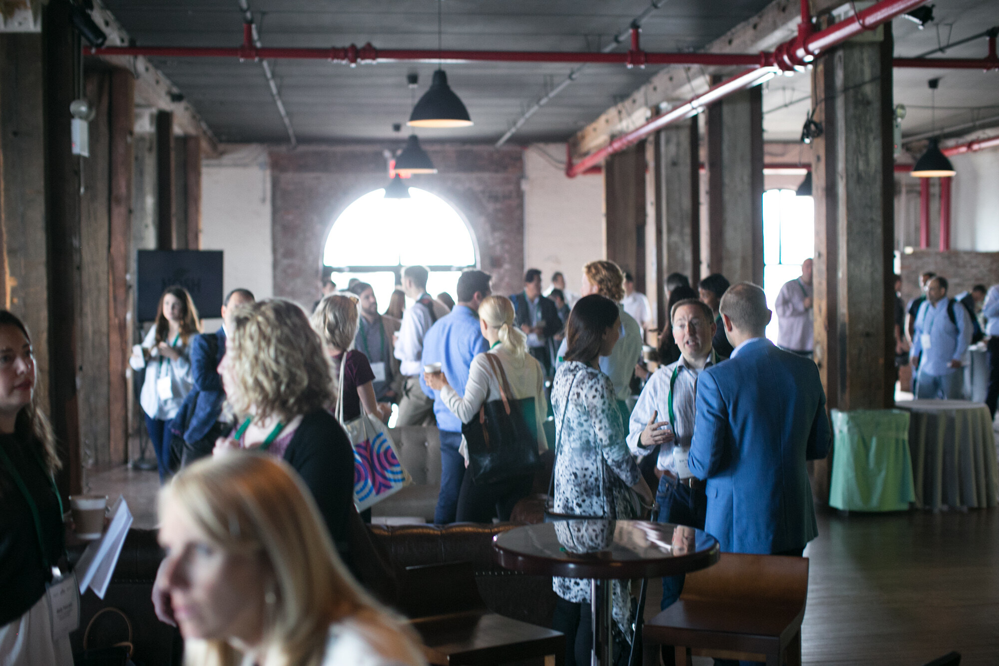 Crowd of attendees in a brick-walled hall with exposed pipes and an arched window.