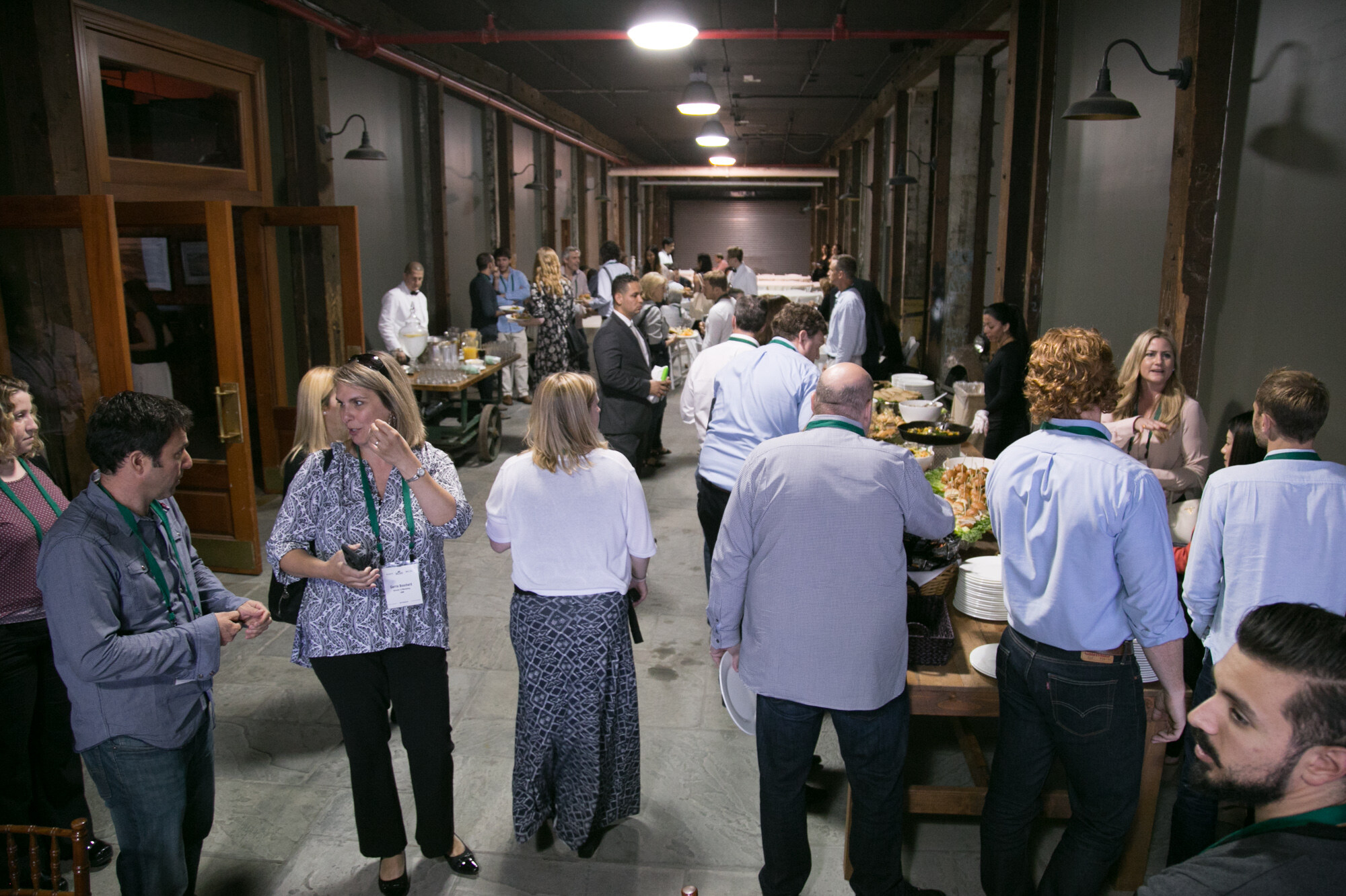 Long hall with buffet tables and attendees wearing green lanyards holding plates.