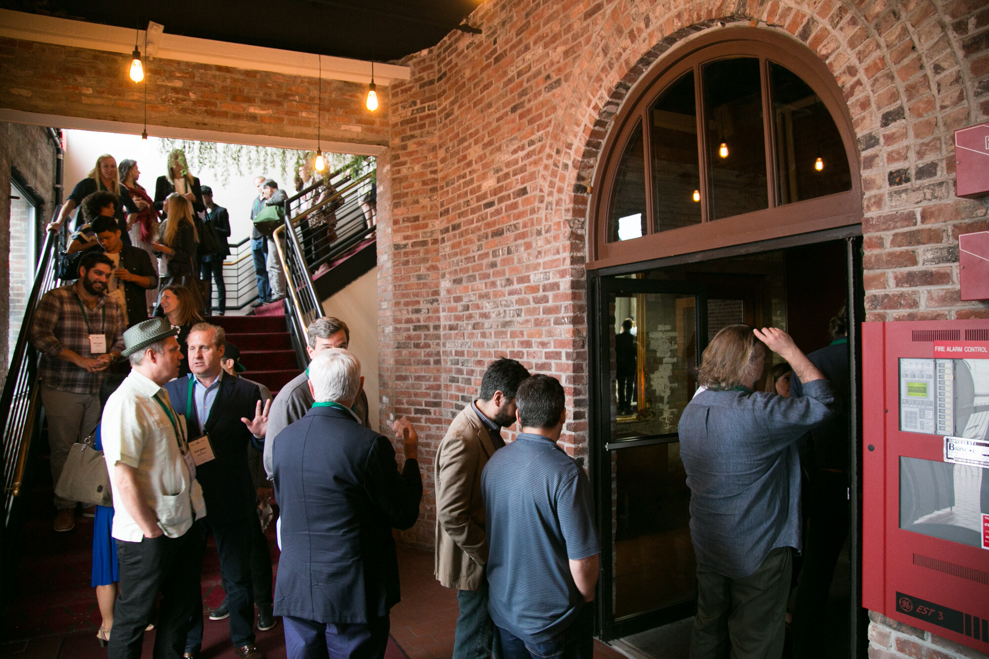 Group of attendees standing inside a red brick entrance with an arched window and stairs behind them.