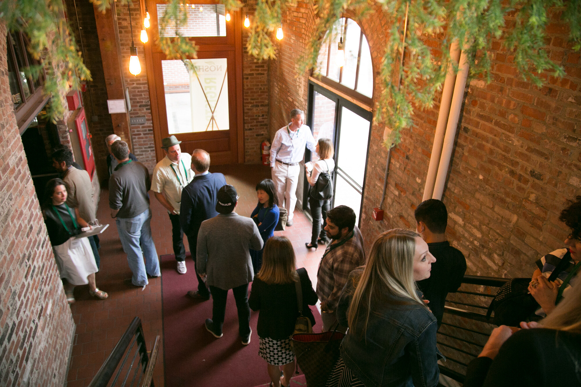 Overhead view of attendees standing on a red-carpeted stairway lined with brick walls and hanging greenery.