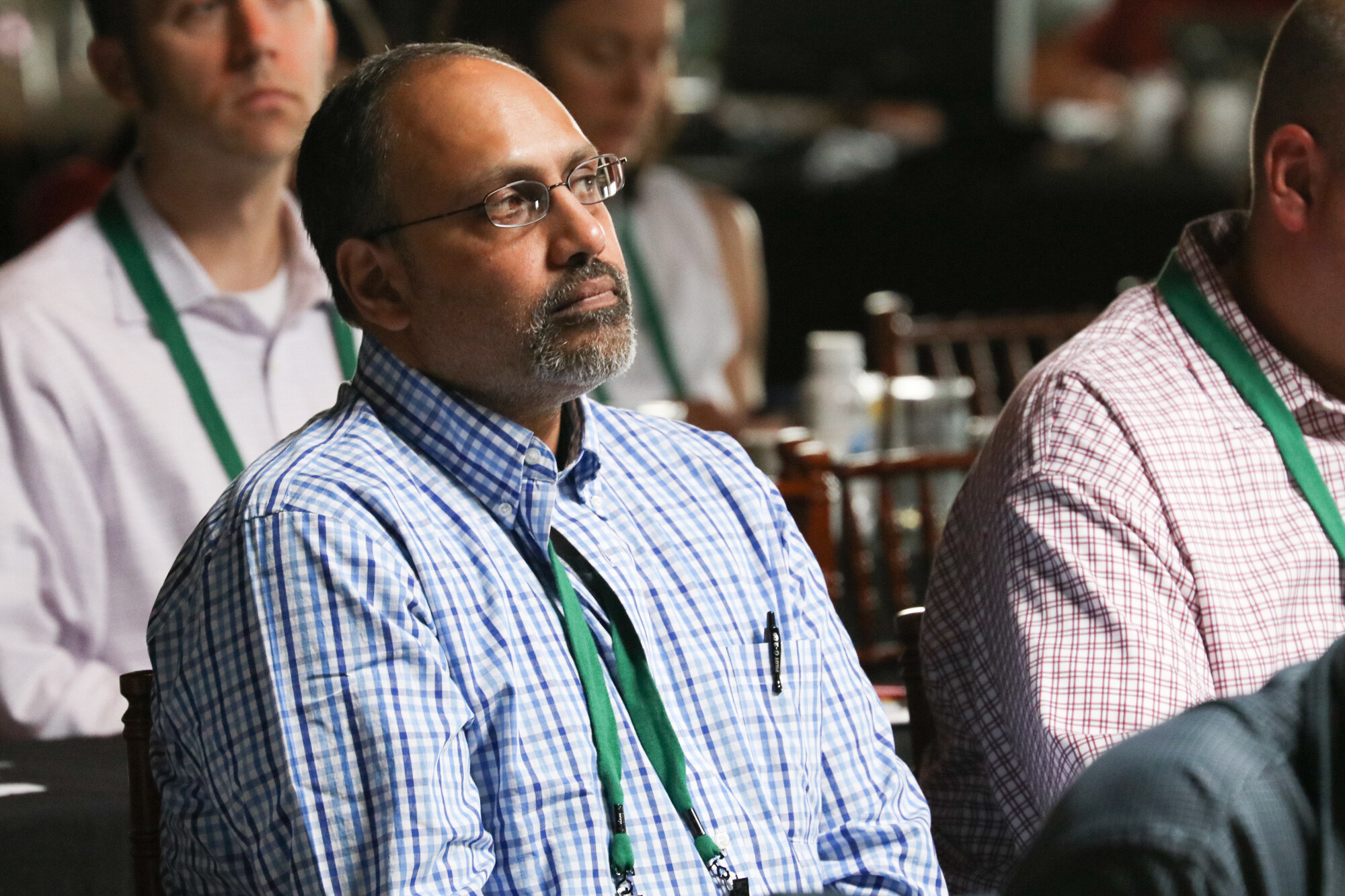 Close view of three seated attendees with green lanyards looking toward the stage.