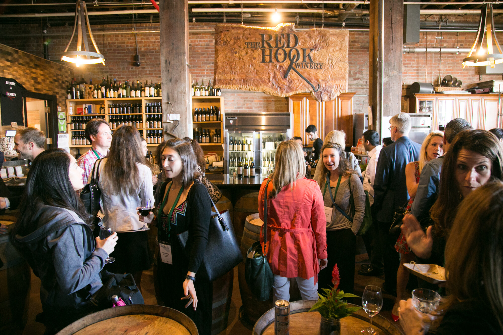 Crowd of guests with wine glasses in front of the bar and a carved Red Hook Winery sign.