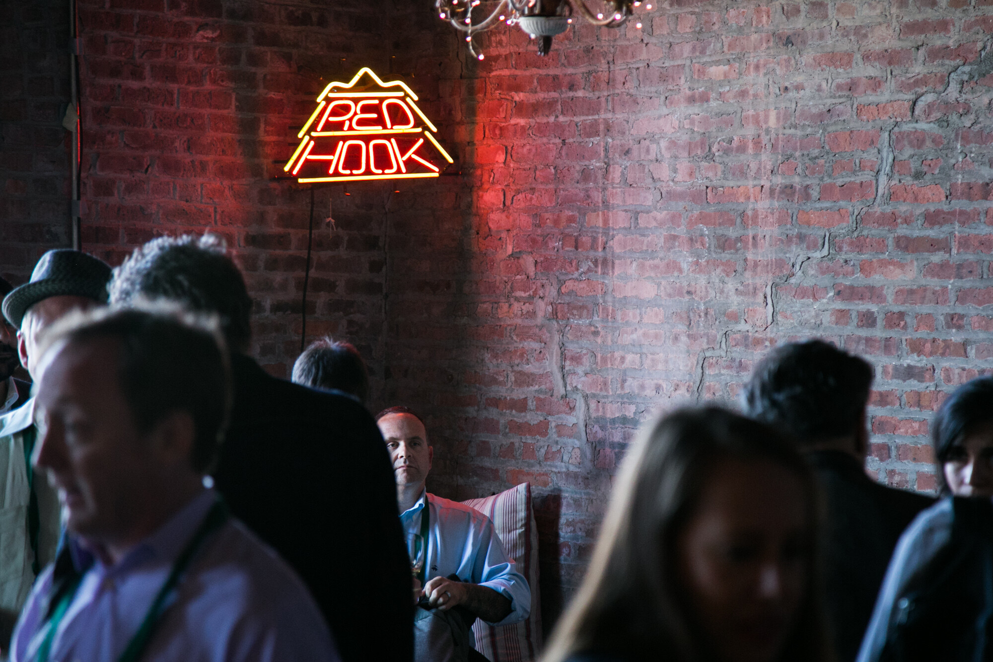 Orange neon sign reading Red Hook on a red-lit brick wall with guests in the foreground.