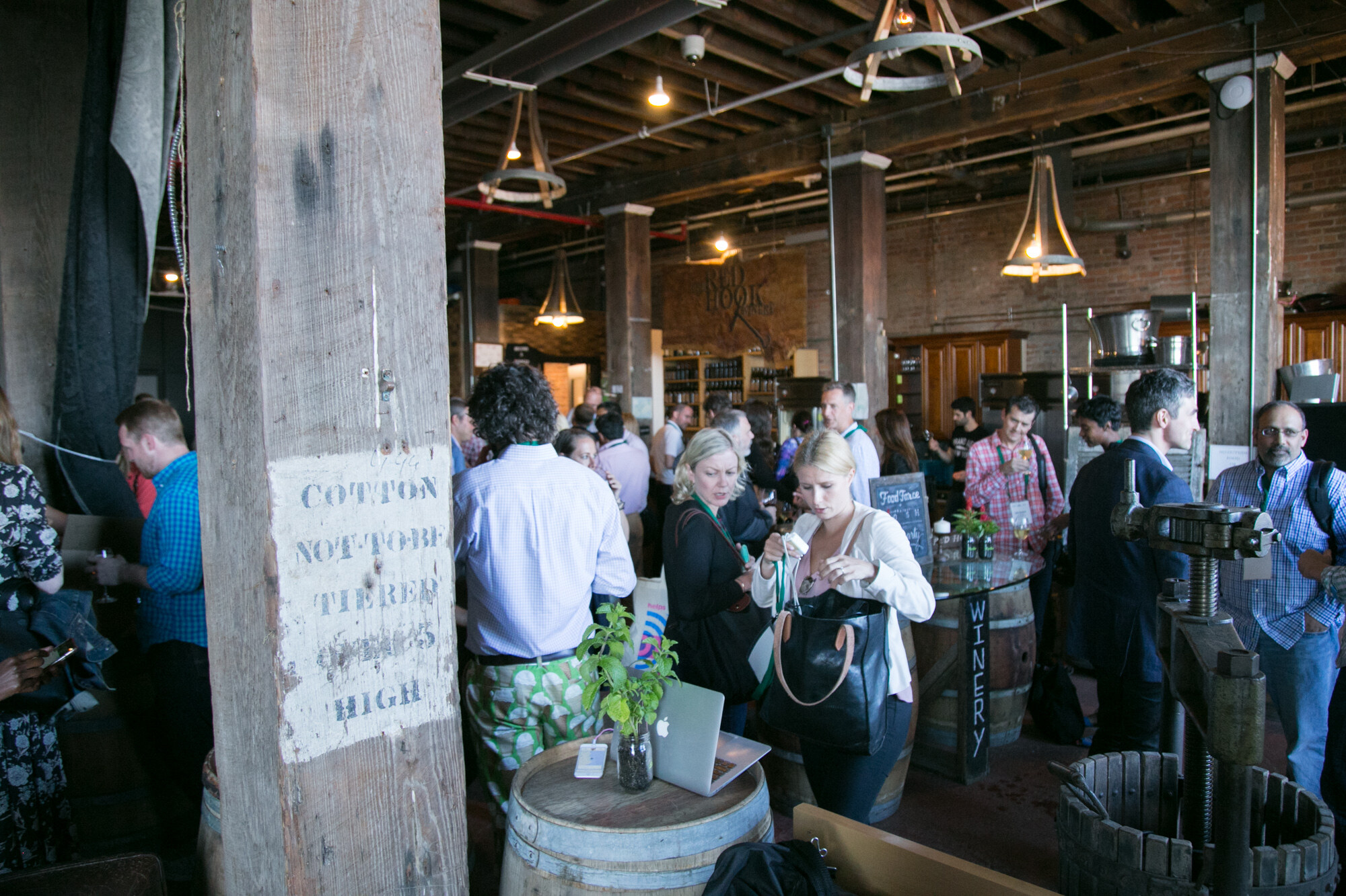 Crowd of guests in the winery with a stencilled wooden post, barrel tables and a wine press.