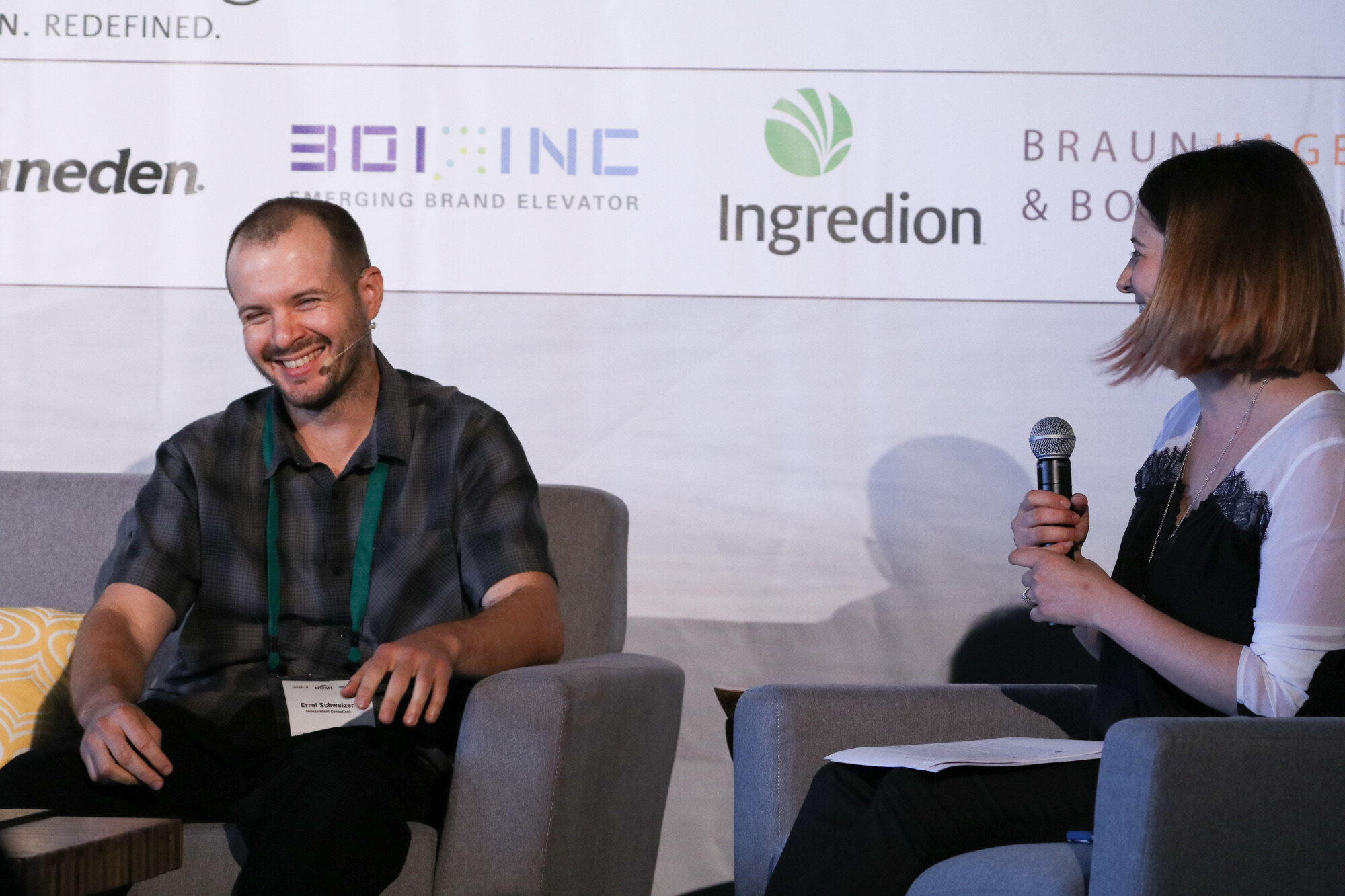 Smiling man in a checked short-sleeve shirt seated in a gray armchair, with a woman holding a microphone on the right, under a banner showing Ingredion and Braun Hagey logos.