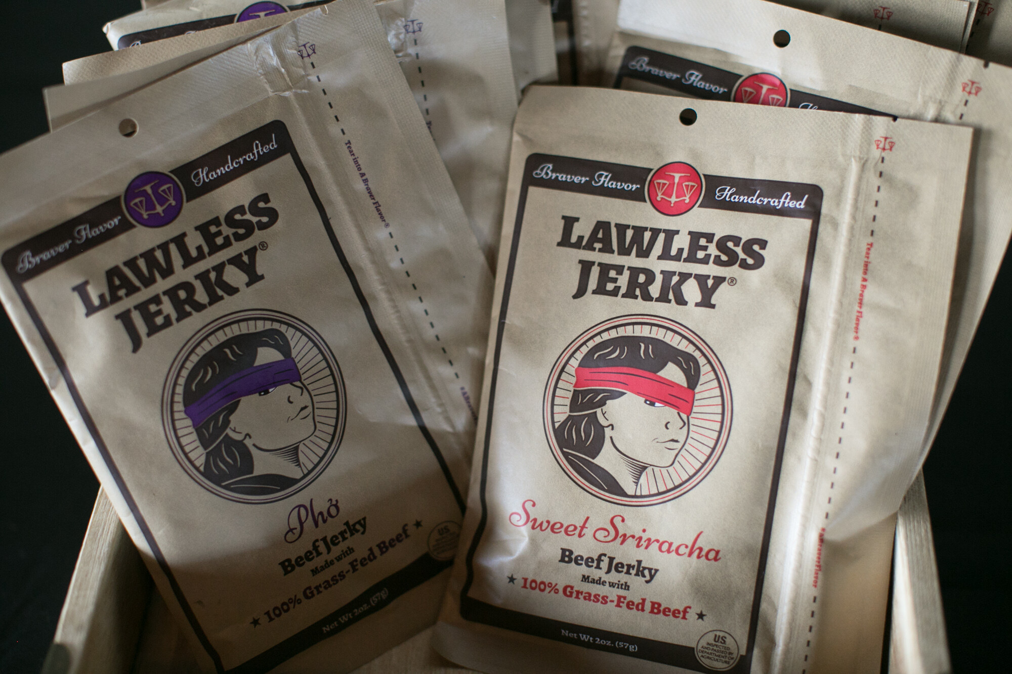 Tan bags of Lawless Jerky, Pho and Sweet Sriracha beef jerky made with grass-fed beef.