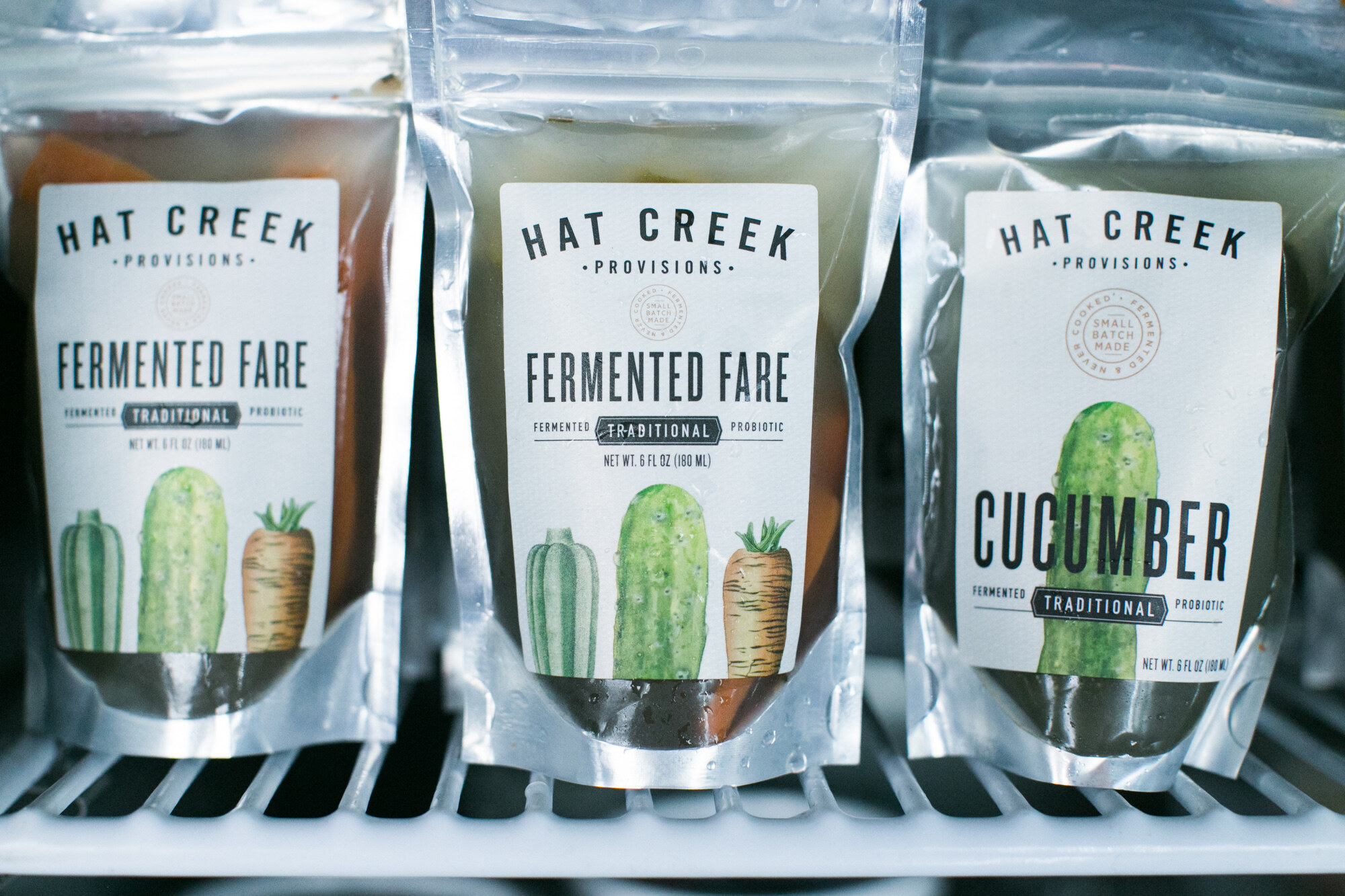 Three silver pouches labeled Hat Creek Provisions Fermented Fare and Cucumber on a cooler shelf.