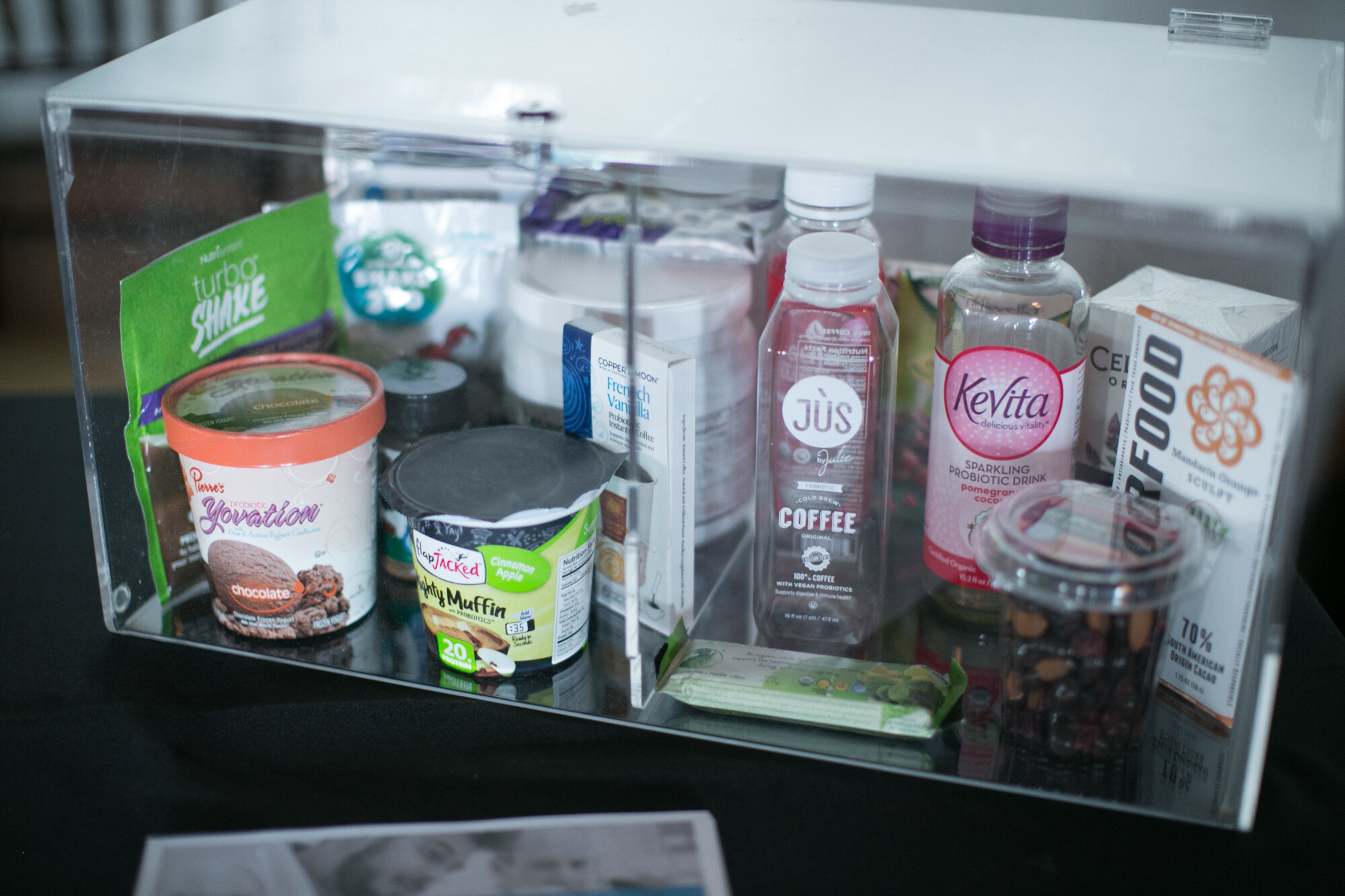 Clear acrylic case with Turbo Shake, Yovation ice cream, SlimJacked muffin cup, Jus coffee, KeVita sparkling probiotic drink and a nut mix.