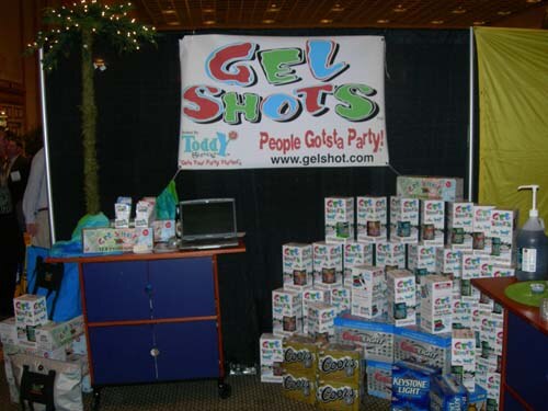 Gel Shots booth with a black backdrop and a Gel Shots banner reading People Gotsta Party, with stacked boxes of product, a laptop on a blue cabinet, and Coors and Keystone Light cases below.