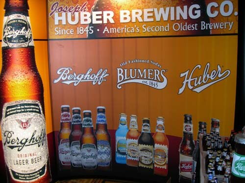 Orange display wall for Joseph Huber Brewing Co. showing Berghoff, Blumers and Huber logos, with Berghoff and Blumers bottles pictured and real bottles at the right edge.