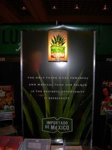 A dark display panel with an agave plant image and a lit Pulque La Lucha sign, with text about the business opportunity and an 'Importado de México' label.