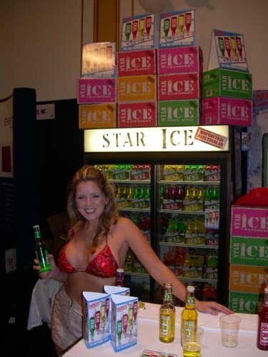 A smiling woman in a red top holds a green bottle beside a Star Ice refrigerated display, with stacked Ice boxes above and bottles on the counter.