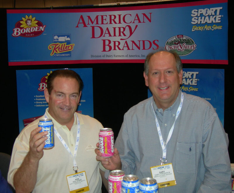 Ken Adams, left, and Gary Frederick of American Dairy Brands, right, hold Sport Shake cans in front of an American Dairy Brands banner with Borden, Keller's and Cache Valley logos.