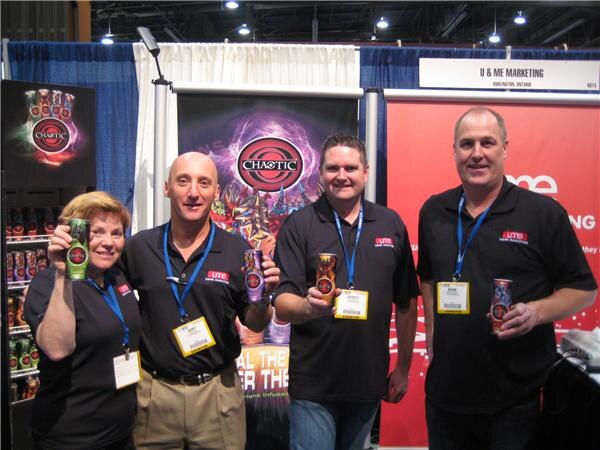 Two men and a woman in black polo shirts pose with a fourth man, each holding a can of Chaotic, in front of a Chaotic banner and U & ME Marketing sign.