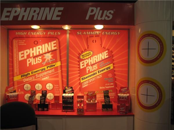 A red and orange booth wall with large Ephrine Plus graphics for High Energy Pills and Slammin' Energy liquid sport pack, with small product displays on a ledge below. No people are visible.