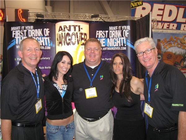 Five people with badges, three men and two women, pose together in front of Resurrection anti-hangover banners; a Redline banner is visible behind them.
