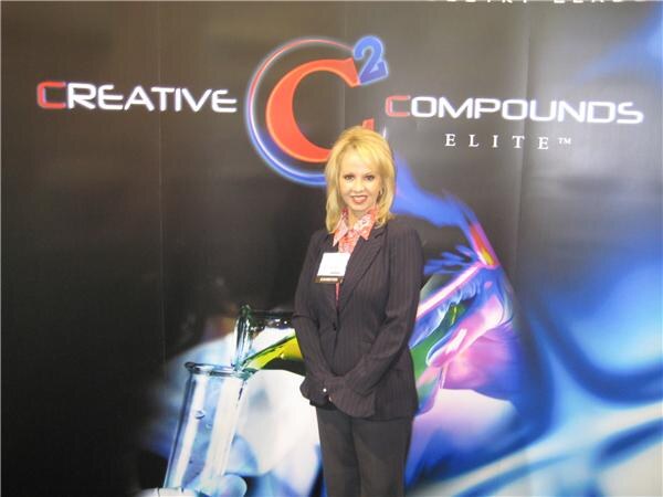 A blonde woman in a dark pinstripe suit with a badge stands in front of a dark Creative Compounds Elite backdrop showing a glowing logo and a glass beaker.