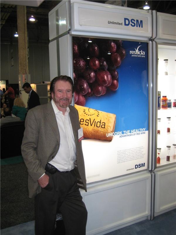 A bearded man in a tweed blazer stands beside a lit DSM display showing grapes and a cork, with the resVida logo and the line 'Uncork the healthy advantages of red wine'.