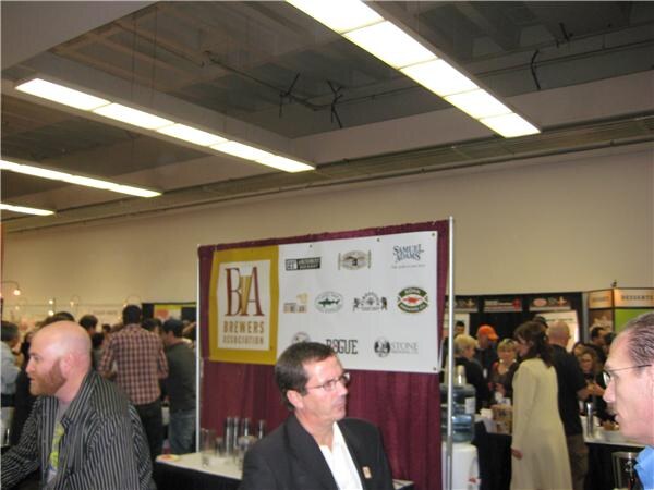 A Brewers Association banner lists logos including Samuel Adams, Rogue and Stone, with several attendees standing in the busy hall around it.