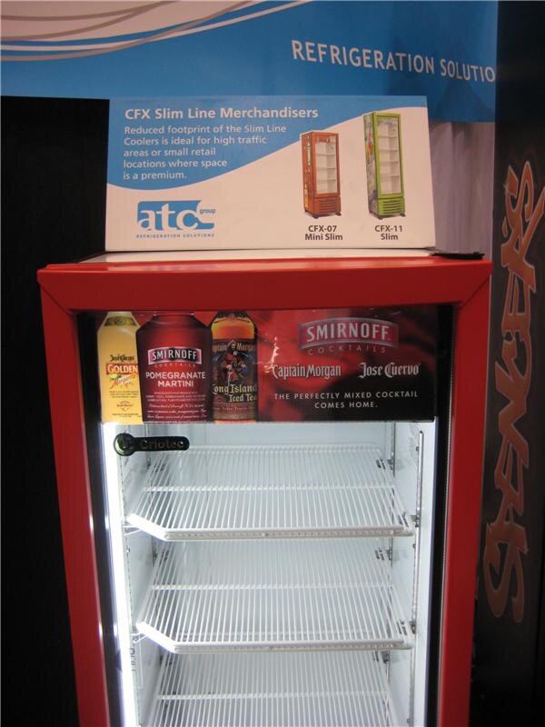 A red-framed slim cooler with empty shelves under a Smirnoff, Captain Morgan and Jose Cuervo header. A sign above reads CFX Slim Line Merchandisers from atc group.