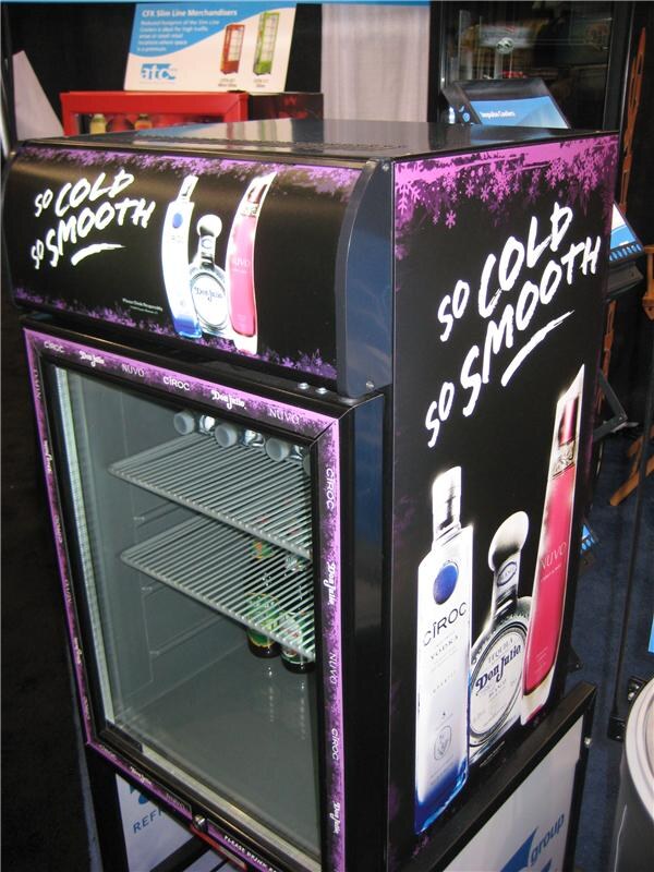 A black and purple glass-door cooler reading "So cold so smooth" with bottles of Ciroc, Don Julio and Nuvo pictured on its sides and top. An atc group sign sits behind it.