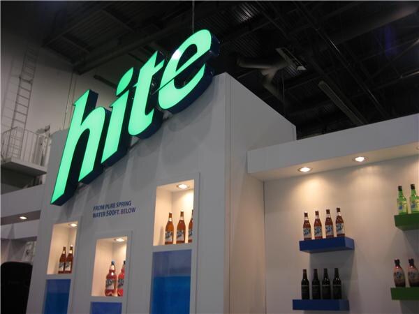 A glowing green Hite sign on a white booth wall above lit shelves displaying bottles of Hite beverages.