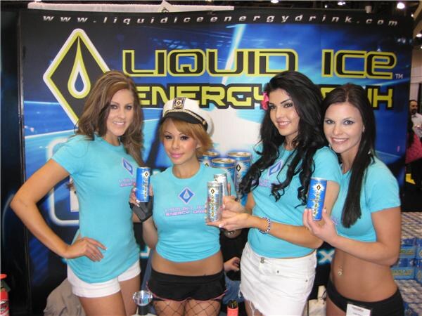 Four women in light blue Liquid Ice shirts, one wearing a captain's hat, hold cans of Liquid Ice Energy Drink in front of a blue and yellow Liquid Ice banner.