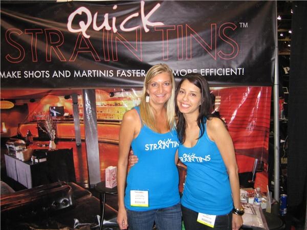 Two smiling women in blue Quick Strain Tins tank tops and badges stand arm in arm beneath a banner reading Make shots and martinis faster and more efficient.