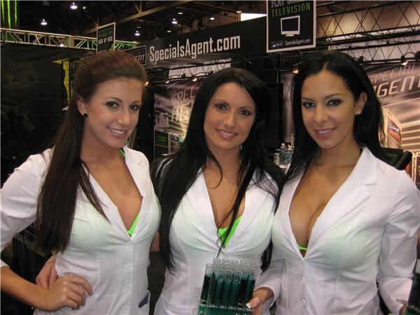 Three smiling women with long dark hair in white jackets stand together under a SpecialsAgent.com banner. One holds a rack of green-filled test tubes.